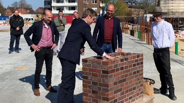 Sonnenschein bei der Grundsteinlegung: Landrat Florian Lorenzen am ersten Mauerwerk, Bürgermeister Uwe Schmitz und Adelby-1-Geschäftsführer Heiko Frost gucken zu.