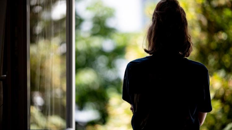 ARCHIV - Eine Frau steht in ihrer Wohnung am Fenster. Foto: Fabian Sommer/dpa/Illustration