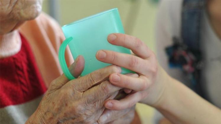 Eine Pflegerin hilft einer Seniorin beim Trinken. 