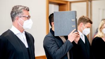 Der Angeklagte steht vor der Prozessfortsetzung in einem Saal im Landgericht und bedeckt sein Gesicht mit einem Aktenordner. Foto: Hauke-Christian Dittrich/dpa