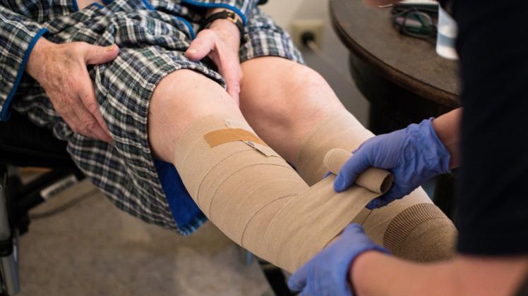 ARCHIV - Eine ambulante Pflegerin bandagiert die Beine eines alten Mannes. Foto: Jana Bauch/dpa