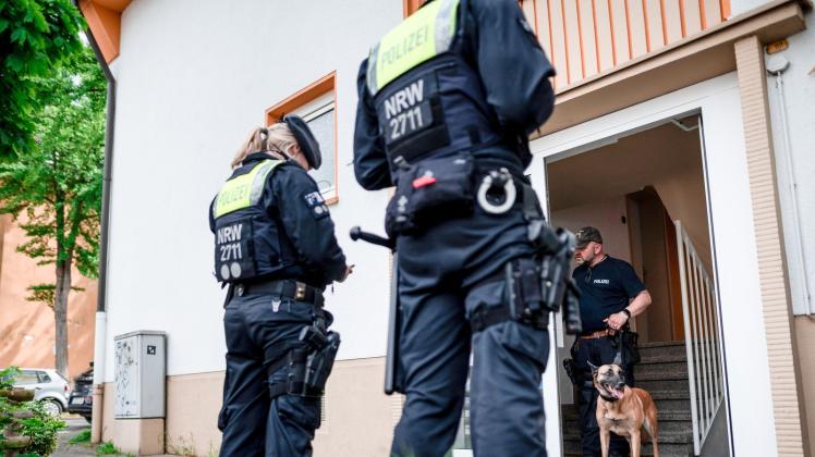 Ein Polizist mit Spürhund steht im Hauseingang des Tatverdächtigen in Essen. Foto: Fabian Strauch/dpa