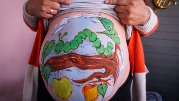 Die Hobbymalerin Marienn Pyko hat der Schwangeren Sandra Genz eine kleine hungrige Raupe auf den Babybauch gemalt. Foto: Jens Büttner/dpa - ACHTUNG: Nur zur redaktionellen Verwendung im Zusammenhang mit der aktuellen Berichterstattung und nur mit vollständiger Nennung des vorstehenden Credits