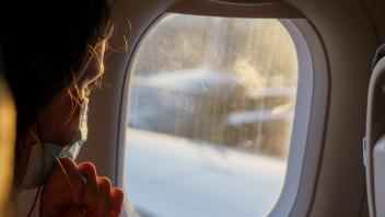ARCHIV - Ein weiblicher Fluggast mit Maske schaut vor dem Start aus dem Fenster. Auf Flügen von und nach Deutschland muss weiter Maske getragen werden. Foto: Andreas Arnold/dpa
