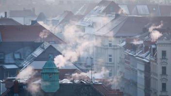ARCHIV - Rauch strömt aus Kaminen auf Dächern von Mehrfamilienhäuser. Foto: Jan Woitas/dpa