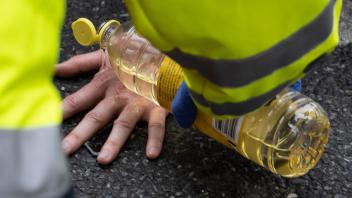Ein Feuerwehrmann übergießt die Hand eines Aktivisten der Gruppe "Letzte Generation" mit Sonnenblumenöl. Foto: Swen Pförtner/dpa