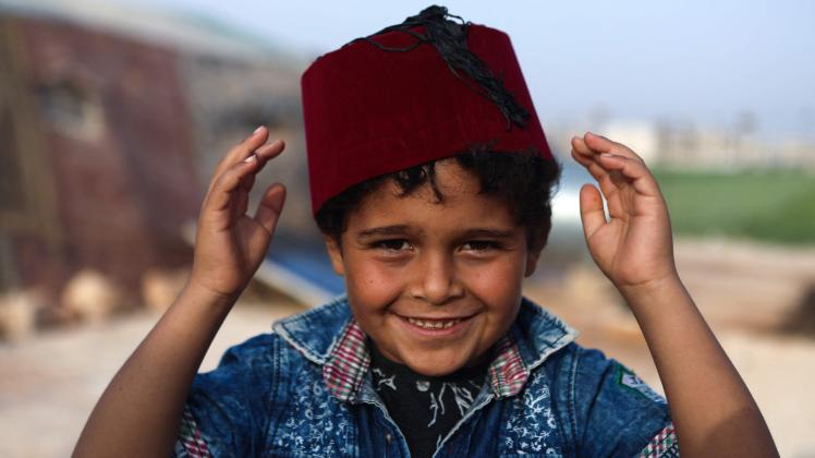 A boy wears a fez as Syrian volunteers in traditional Damascene confectioner's outfits distribute sweets to families at a camp for the internally displaced on the outskirts of the rebel-held town of Dana, in the northwestern Idlib province near the Turkish-Syrian border, on May 1, 2022, on the eve of Eid al-Fitr which marks the end of the holy fasting month of Ramadan. (Photo by Aaref WATAD / AFP)