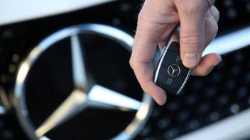Mercedes Benz, Stern, Logo, auf einem Mercedes Benz Fahrzeug, davor eine Hand mit Autoschluessel und Mercedes Benz Logo