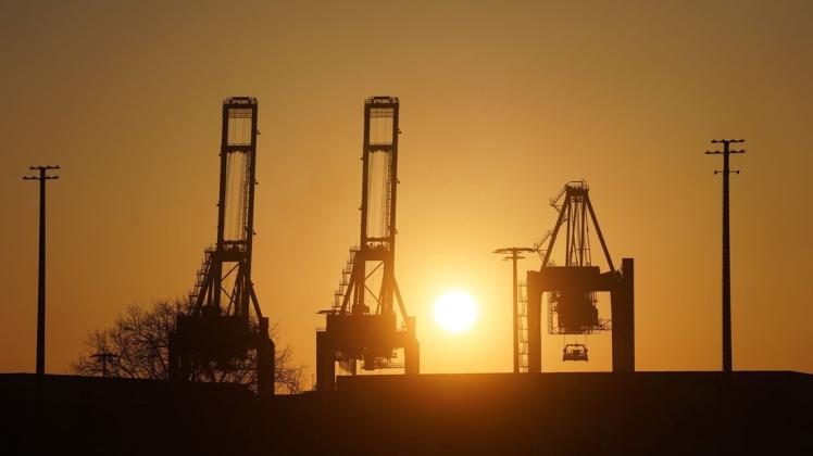 Die Sonne geht über den Containerbrücken im Hamburger Hafen auf.
