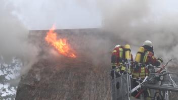 Feuerwehrleute auf einer Drehleiter löschen die Flammen an einem Reetdach in Badbergen.