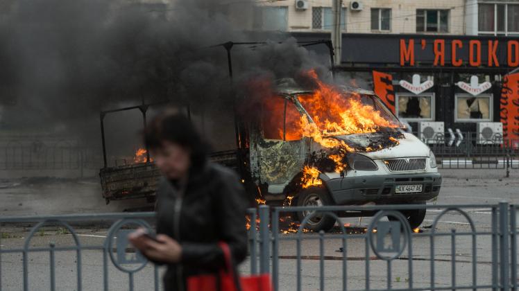 An Ukrainian woman walks in front of a truck in flames after a shelling by the Russian forces in Kharkiv, Ukraine, 26 Ma