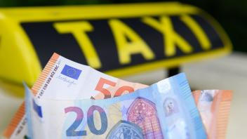PRODUKTION - Eine Person hält Geldscheine vor einem Taxi-Schild auf einem Taxi. Foto: Jonas Walzberg/dpa/Illustration