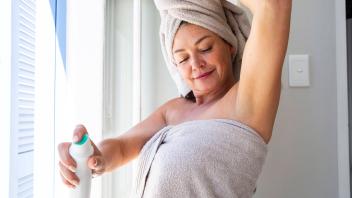Smiling woman wearing towel spraying deodorant on body at home model released, Symbolfoto property released, ESTF00025