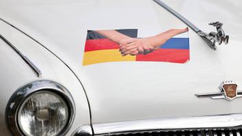 Ein Oldtimer der russischen Marke Wolga ist mit russischen und deutschen Flaggen verziert. Vor dem Hintergrund des Krieg