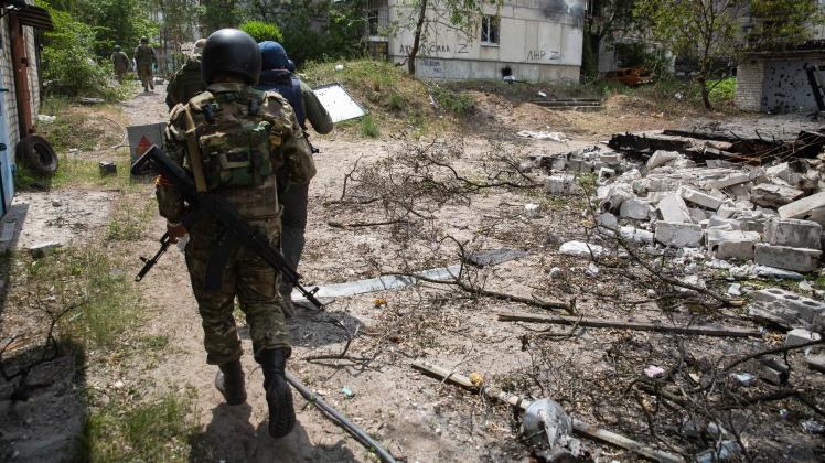 LUGANSK REGION, UKRAINE - MAY 29, 2022: Akhmat special unit servicemen walk past apartment buildings damaged by shellin