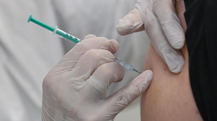 ARCHIV - Ein Mitarbeiter eines Impfzentrums impft einen Mann gegen Corona. Foto: Patrick Pleul/dpa-Zentralbild/dpa/Symbolbild