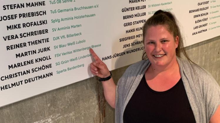 author Marlene Knoll zeigt auf ihren Namen an der Ehrenwand der Preisträger des Club 100 des DFB.