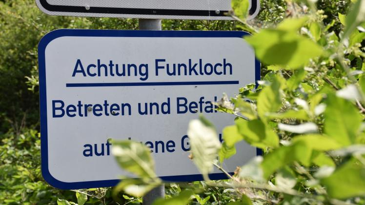 Ein Schild mit der Aufschrift „Achtung Funkloch“ wird von einigen Blättern bedeckt.