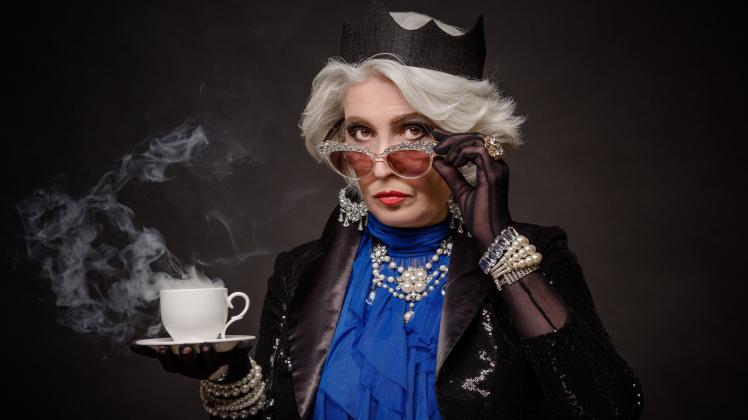 Senior rich woman having a cup of tea as Queen Elizabeth from Great Britain. Beautiful old lady in expensive clothing isolated on black. (Lipik)