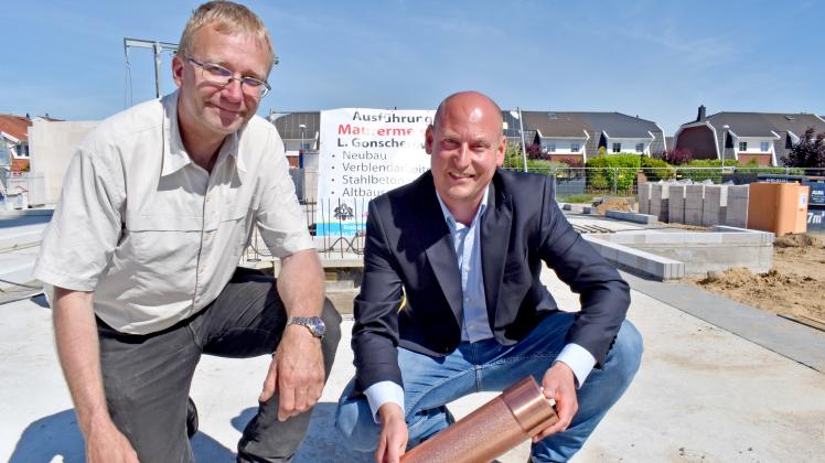 Bürgermeister Matthias Eberhardt (l.) und Bauherr Martin Jaskulke haben die Zeitkapsel für die Wohnanlage befüllt und legen sie nun in das Fundament. 