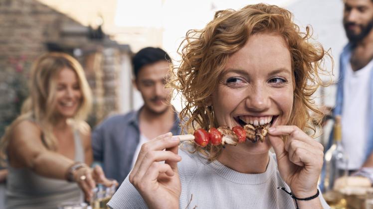 Young woman eating meat skewer at a backyard patry with friends model released Symbolfoto property r