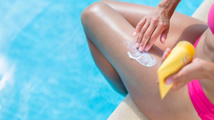 Attractive, young woman with healthy skin applying suncream by a pool (shallow DOF color toned image) ,model released,