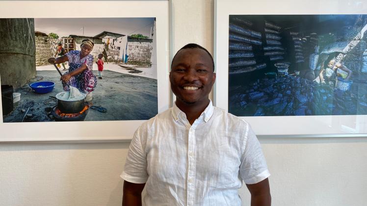 Der Fotokünstler Imani Nsamila vor zwei seiner Fotos zum Thema illegaler Holzabbau.