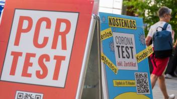 Schilder mit der Aufschrift «PCR Test» und «Corona-Test - Kostenlos» hängen vor dem Eingang einer Apotheke in der Innenstadt von München. Foto: Peter Kneffel/dpa