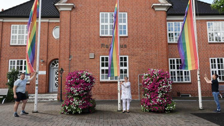 author Nils Bollenbach (v.l.), Bürgervorsteherin Cornelia Harmuth und Gerrit Kronenberg hissen drei Regenbogenflaggen vor dem Bargteheider Rathaus.