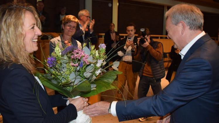 Der amtierende Bürgermeister Jörg Sibbel überreicht seiner am 29. Mai per Stichwahl gewählten Nachfolgerin Iris Ploog (SPD) einen Blumenstrauß.  Im Hintergrund die von CDU, Grünen und FDP unterstützte Gegenkandidatin Jenny Kannengießer