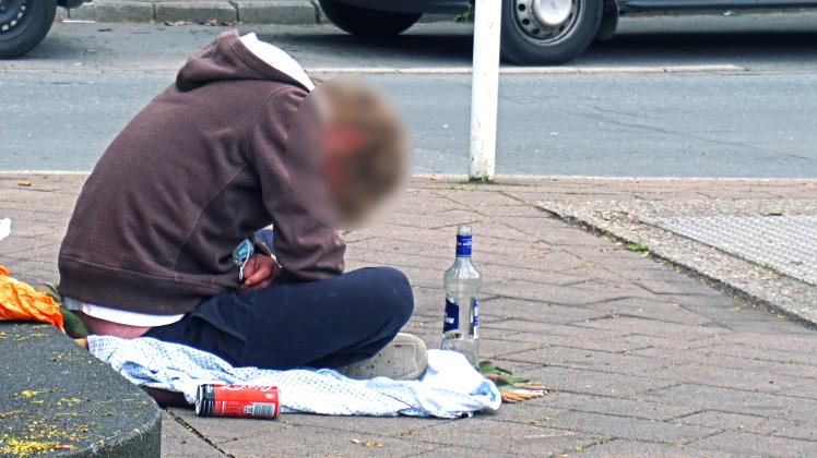 Armutsschicksale in Deutschland Eine obdachlose Person sitzt mit einer entleerten Flasche Vodka auf dem Boden und droht