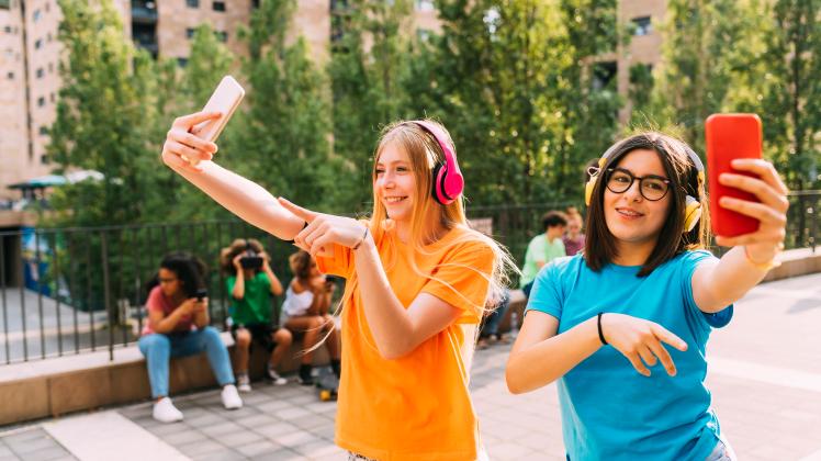 Happy girls wearing wireless headphones filming through smart phone model released, Symbolfoto, MEUF06212
