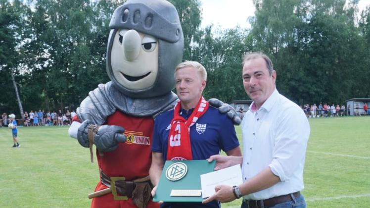 Verein Wacker-Vorsitzender Ramon Schaefer (M.) mit der DFB-Ehrenplakette. Eingerahmt von Keule, Maskottchen des 1. FC Union Berlin und Marcel Elverich vom Fußballkreis Prignitz-Ruppin.
