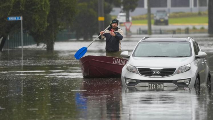 Ein Mann paddelt mit seinem Boot auf einer überfluteten Straße am Stadtrand von Sydney. Foto: Mark Baker/AP/dpa