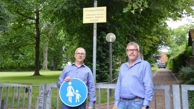 Zwei Männer stehen am Eingang eines Parks unter einem „Betreten verboten“-Schild