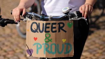 Ein Mensch mit Schild Queer & Proud während einer Regenbogen-Fahrraddemo für mehr queere Sichtbarkeit in Potsdam, 2. Ju