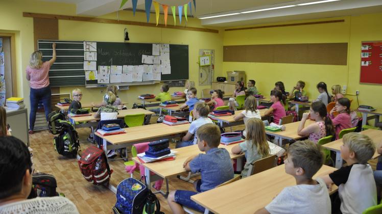 28 Schüler und eine Schulbegleiterin sitzen in der 1. Klasse in einem Klassenzimmer eng beieinander.