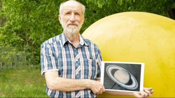 Tour-Guide und Physiker Dr. Stephan Bakan verdeutlicht die Größenunterschiede: Die kleine blaue Kugel in seiner Hand stellt die Erde dar, daneben eine Abbildung des Saturns und im Hintergrund die große Sonne. 