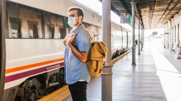 Young man with backpack standing on railroad station platform during pandemic model released Symbolfoto property release