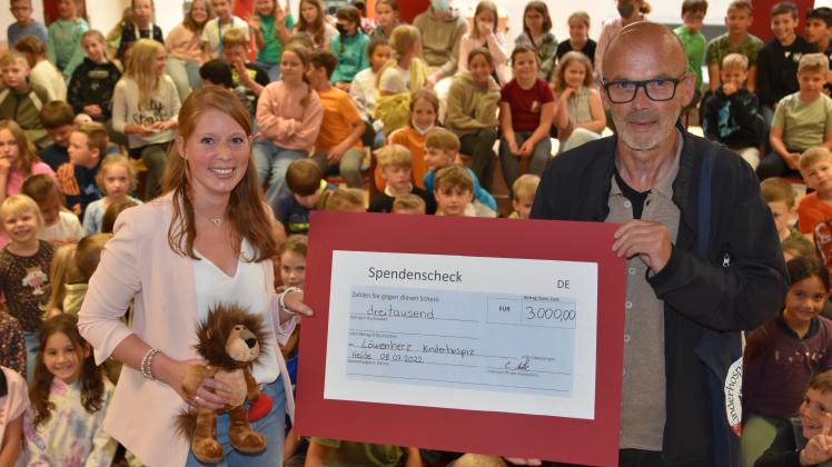 Schulleiterin Cathrin Witte übergibt den symbolischen Spendenscheck im Beisein der Schülerschaft an Löwenherz-Ehrenamtler Siegfried Held.  