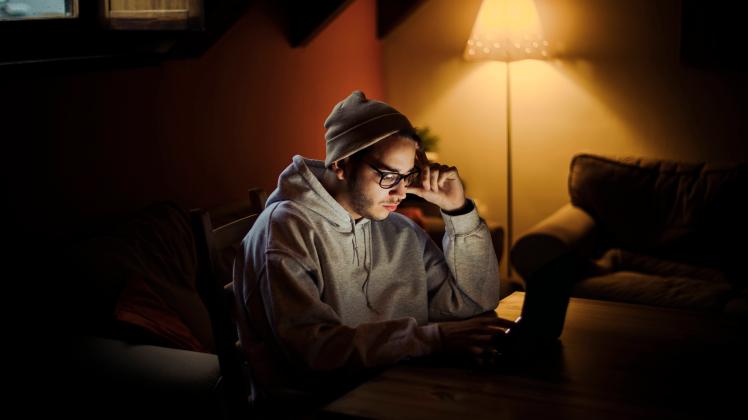 Man with head in hands using laptop in darkroom at home model released Symbolfoto ACPF01224