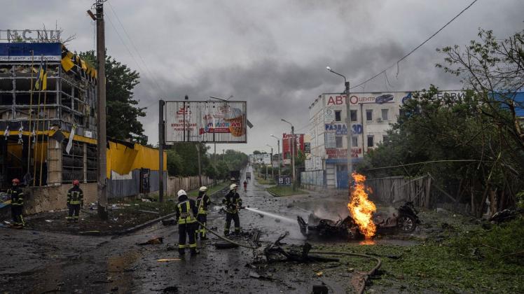 Feuerwehrleute löschen  nach einem russischen Angriff in der Innenstadt von Charkiw das Feuer eines zerstörten Autos. Foto: Evgeniy Maloletka/AP/dpa