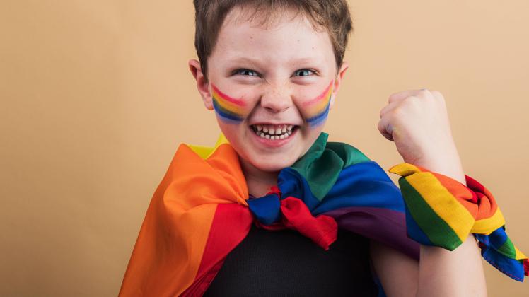 Cheerful kid with makeup on cheeks with LGBTQ flag while looking at camera on beige background HodeiUnzueta_EtxahumStudi