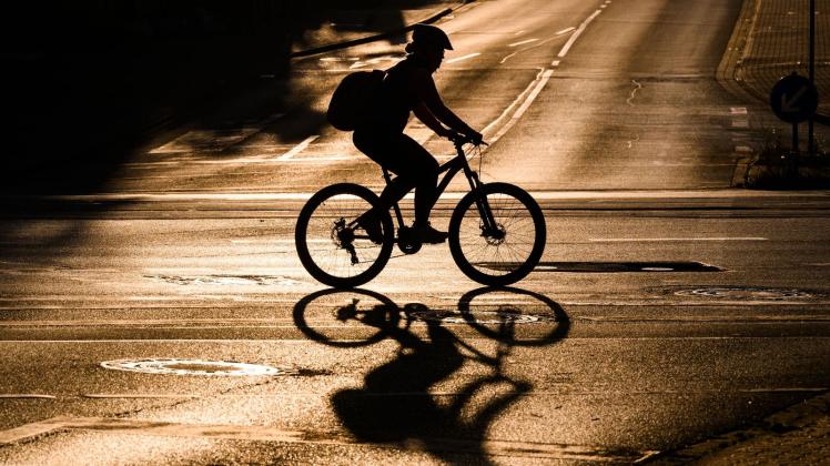 Eine Fahrradfahrerin fährt bei Sonnenaufgang über eine Straße. Foto: Julian Stratenschulte/dpa/Symbolbild