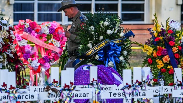 (FILES) In this file photo taken on May 28, 2022, a police officer stands near the makeshift memorial for the shooting victims outside Robb Elementary School in Uvalde, Texas. - Texas state lawmakers on July 17, 2022, slammed law enforcement&apos;s slow response to the shooting in Uvalde, where a gunman killed 19 children and two teachers, saying more decisive action could have saved lives. (Photo by CHANDAN KHANNA / AFP)