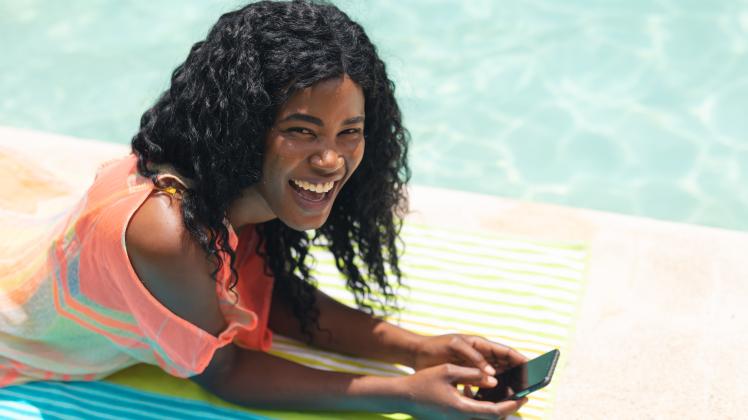 High angle portrait of happy african american mid adult woman with smartphone relaxing at poolside 