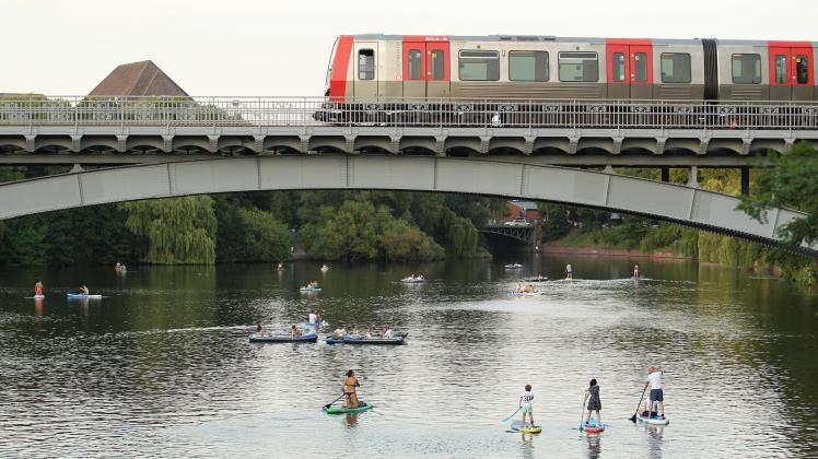 Passanten paddeln auf Stand-up Paddle Boards auf einem Alsterkanal unter einer Brücke entlang, die gerade von einer U-B