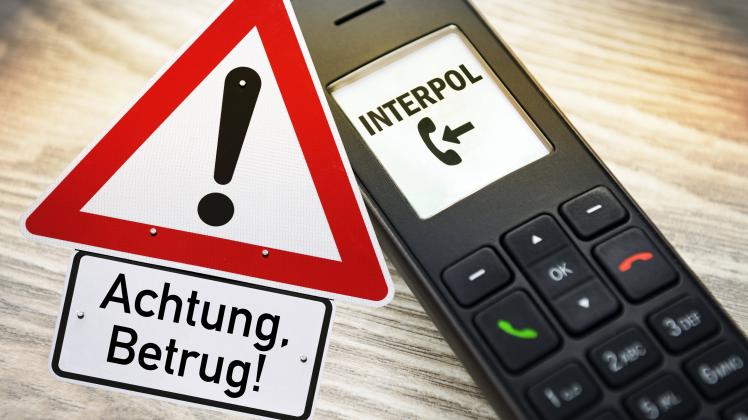 Telefonhörer mit eingehendem Fake-Anruf von Interpol und Schild mit Aufschrift Achtung, Betrug, Symbolfoto Telefonbetrug
