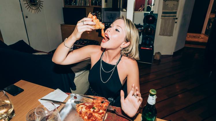Young woman enjoying pizza during party at home model released Symbolfoto property released MEUF01984