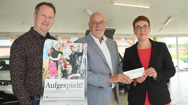 Bürgermeister Johann Hansen (Mitte) aus Schenefeld überreicht die Karten für eine SHMF-Konzert an Torge und Katja Horst. 